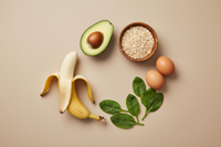 Minimalist premium product photo of a composition of natural ingredients rich in B vitamins: avocado, banana, oats, spinach leaves, and eggs, arranged aesthetically on a soft pastel beige background, diffused natural lighting, clean and elegant flat-lay composition, wellness supplement brand aesthetic, no text, no packaging, harmonious and balanced visual.
